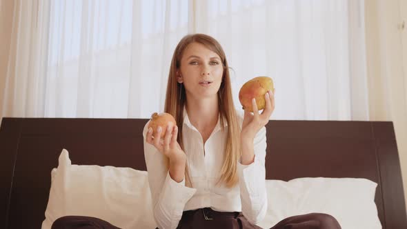 Pleasant Caucasian Woman Holding Pomegranate and Mango in Hands and Talking on