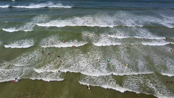 Birds eye drone shot of Muizenberg beach, Cape Town - drone is descending over surfers trying to cat