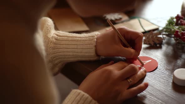 Closeup Back View of Young Woman Writing Number on Red Bag By Brush and White Paint Sitting at Table