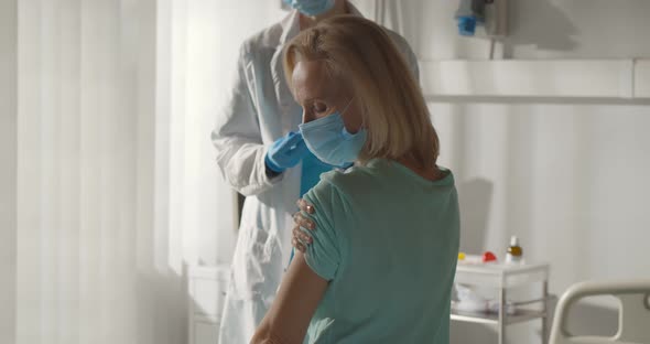 General Practitioner Wearing Protective Mask Vaccinating Mature Female Patient in Clinic