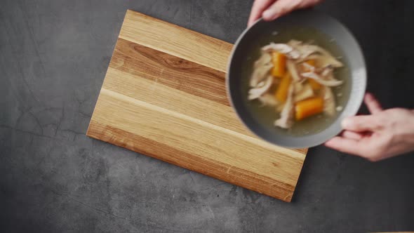 Top view of serving fresh hot healthy paleo chicken broth soup to wooden board on concrete backgroun