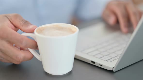 Close Up of Man Drinking Coffee While Using Laptop