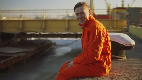 Portrait of Young Worker in Orange Uniform Sitting During His Break By the Sea