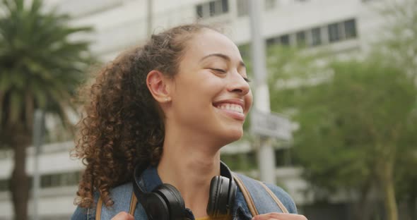 Portrait of happy biracial woman in city, wearing headphones and smiling