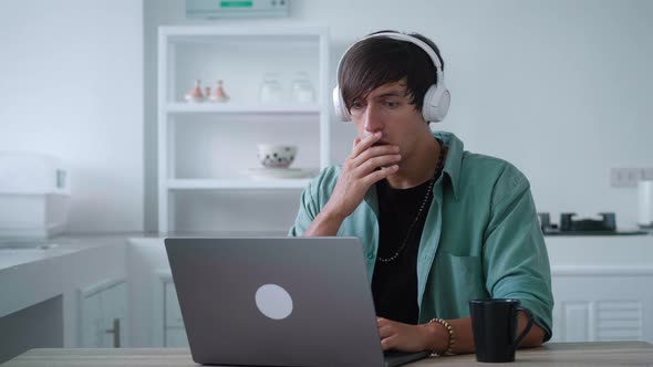 Scared Young Man in Headphones Getting Bad Results on Computer at Home Office