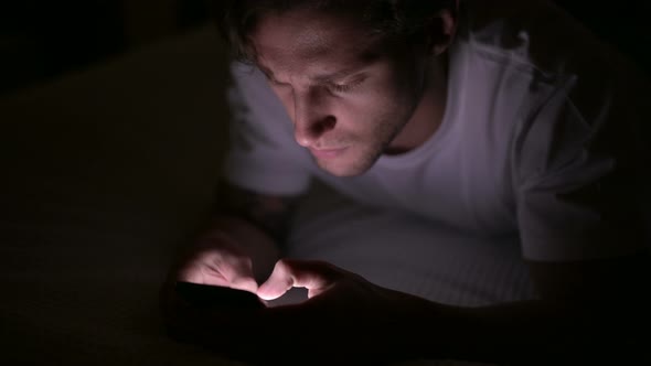 Young Man Using Smartphone in Bed at Night