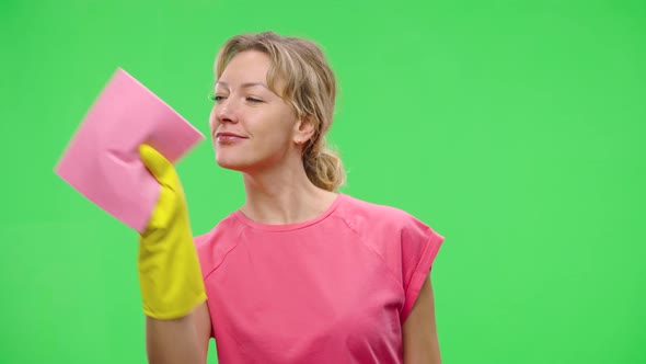 A Young Smiling Woman in Yellow Rubber Gloves Wipes Window Glass with Dry Rag