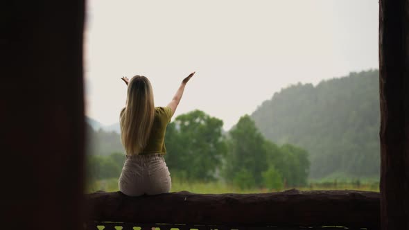 Graceful Woman Catches Drops of Summer Rain Sitting on Log