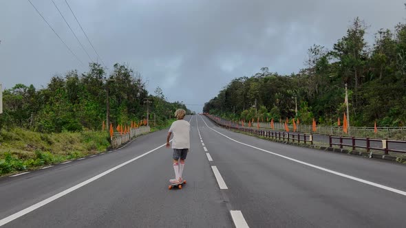 A Young Skateboarder Rides on a Wide Road in a Big City at Sunset