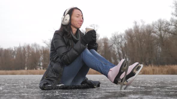 Girl Drinks Coffee and Is Going To Skate, Winter Leisure. Young Woman Ice Skating on a Frozen Lake