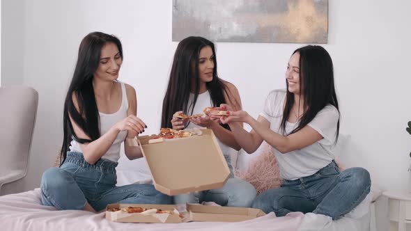 Three Pretty Omen Are Eating Takeaway Pizza in the Bedroom