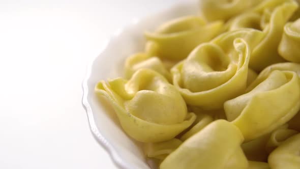 Raw tortellini pasta in a white bowl. Falling in slow motion. Macro