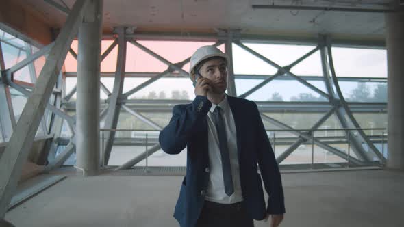 Young Confident Contractor in Elegant Suit on Building Site Talking To Partner on Smartphone