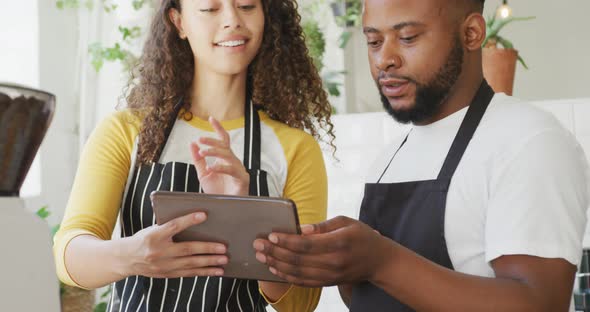 Happy african american male cafe owner and biracial female barista using tablet at cafe