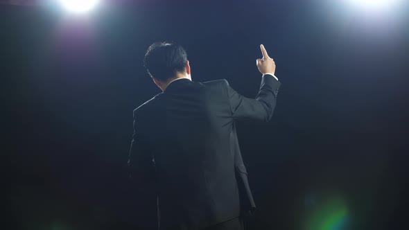 Back View Of Asian Speaker Man In Business Suit Showing Index Fingers Up While Speaking