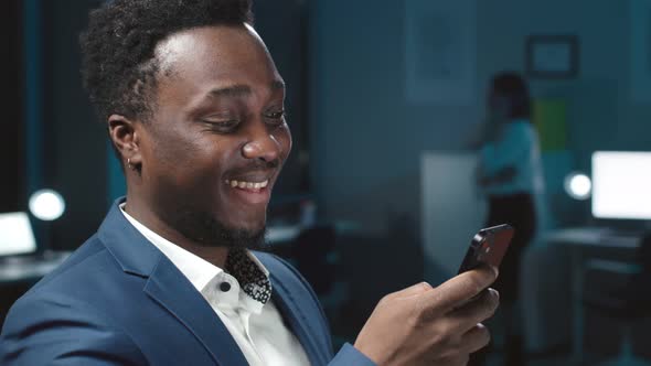 Smiling AfricanAmerican Businessman Chat on Smartphone in Office