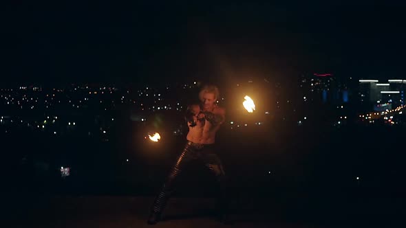 Young Blond Male Naked Torso Spins Two Burning Pois at Night on Black City Background Slow Motion