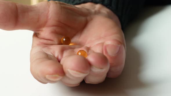 Close-up in the hand of an elderly man transparent round capsules of a pill with omega 3