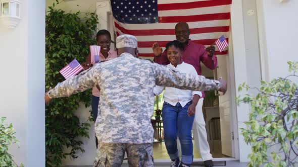 African american soldier father hugging his excited family front of house with american flag