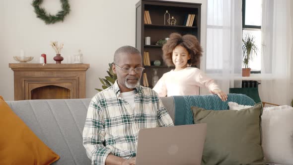 Focused Senior African American Man Working on Laptop at Home Happy Curly Girl Running and Embracing