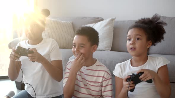 Happy African American Kids Playing Video Game with Joystick at Home