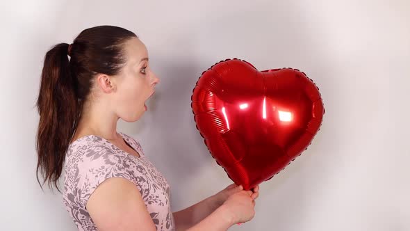 An attractive young female model wearing a cute flowery dress holding up a heart shaped balloon