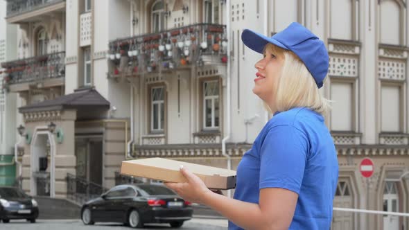 Rear View Shot of a Delivery Woman Looking Around on the Street Holding Pizza Box