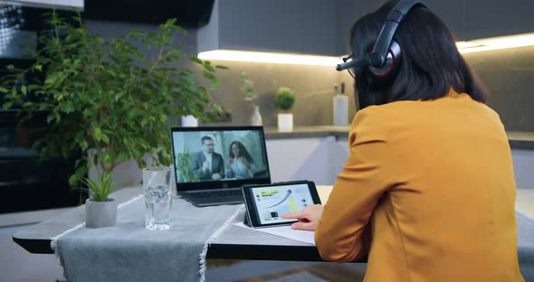 Woman in Headset in Orange Jacket Sitting in front of Computer During Video Meeting