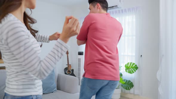 Asian young loving couple dance with music together in living room.