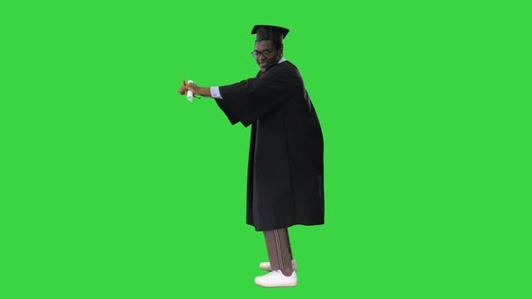 Excited African American Male Student in Graduation Robe Dancing Happily with His Diploma on a Green