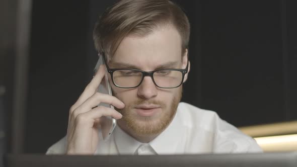 Worried Confident Man in Eyeglasses Talking on the Phone and Looking at Laptop Screen. Close-up