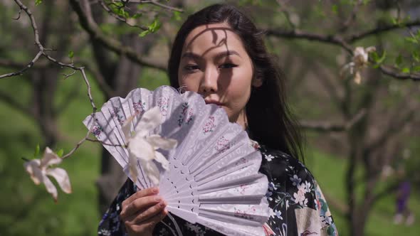 Live Camera Approaches to Confident Asian Beautiful Woman Holding Fan Standing in Blooming Spring