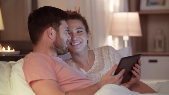 Happy Couple Using Tablet Computer in Bed at Night