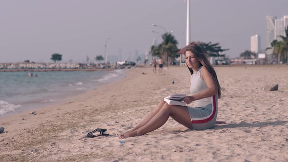 Beautiful Lady with Long Dark Hair Reads Book on Sand Beach