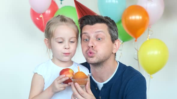 Young Father and Girl with Peach Blow Out Candle on Cupcake