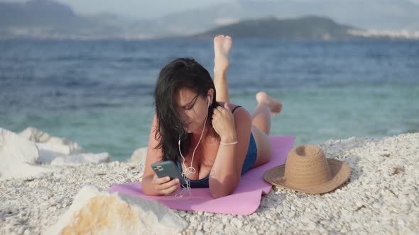 Girl Sunbathing on the Beach and Listening to Music on Headphones