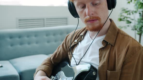 Tiltdown Portrait of Handsome Musician in Headphones Playing Electric Guitar at Home