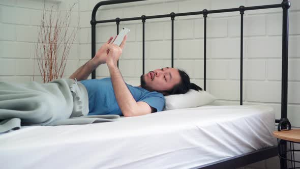 Asia male turn off alarm clock in mobile phone after awake on bed