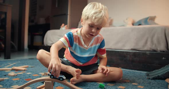 Child Boy Playing with Toy Car on Wooden Railway Road in Living Room on Evening