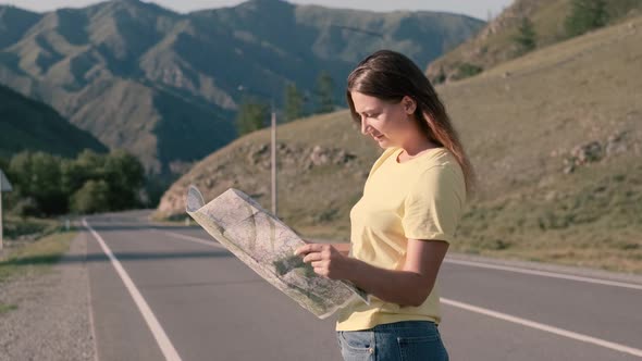 Attractive Female Tourist with a Map in Hand Is Standing on the Highway and Looking for a Route
