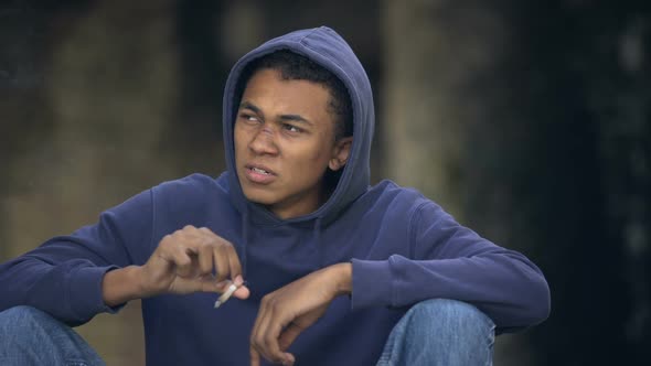 Troubled Teenager With Face Scar Smoking Joint Sitting Street, Dangerous Suburbs