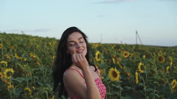 Smiling Beautiful Girl in Summer Dress Poses with Hair in Sunflower Field