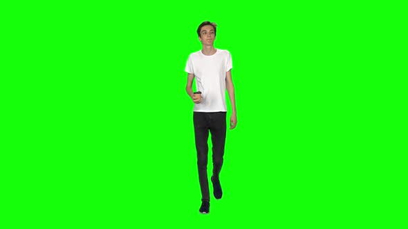 Tall Skinny Teen Guy Calmly Walking and Drinking Coffee on Green Screen. Chroma Key. Front View