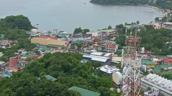 Rotating aerial view of signal tower, sea side surrounded by green trees, houses from the Puerto gal