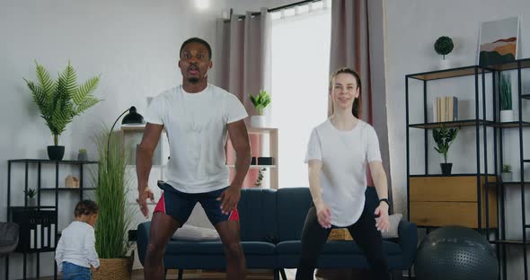 Multiethnic Couple in Training Clothes which Doing Squating Exercises During Home Workout