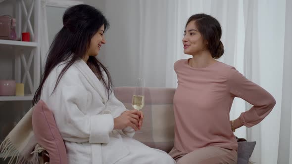 Young Charming Middle Eastern Woman Giving Gift Box for Friend Sitting in Cozy Living Room on Couch