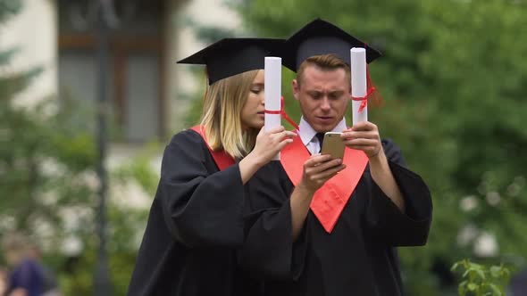 Friends Graduates Wearing Academic Dresses Viewing Photos on Smartphone