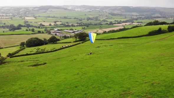Aerial shot following a Paraglider flying in a Valley in Devon England