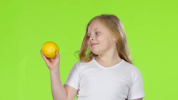 Little Girl Is Holding a Lemon and Sniffing It. Green Screen
