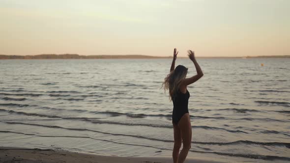 Silhouette Slim Woman Practices Yoga on a Sandy Beach Against Evening Lake